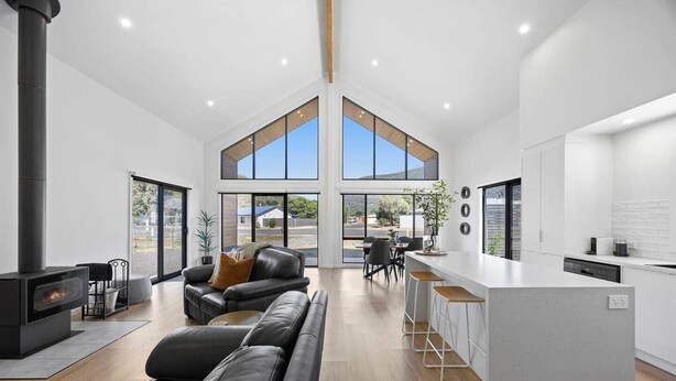 A spacious living area with a black leather sofa, a dining table with chairs, and a kitchen area with a white countertop and bar stools.
