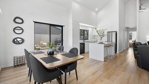 A modern kitchen with white cabinets, a central island with bar stools, and a dining area with a wooden table and black chairs.