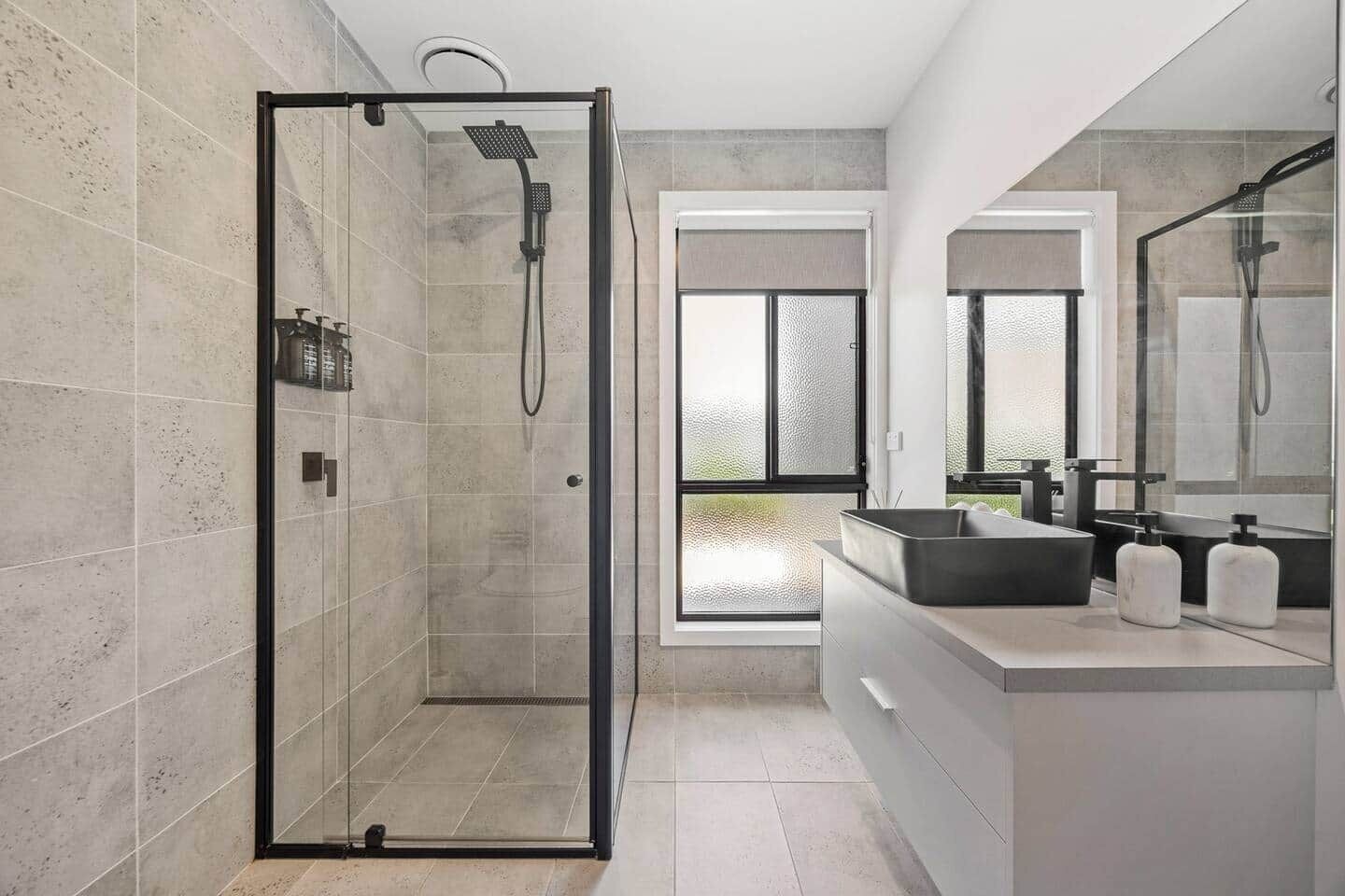 A modern bathroom with a glass-enclosed shower, a large mirror, and a vanity with a sink and soap dispensers.