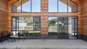 A modern building with a wooden exterior, large glass windows, and a covered outdoor seating area with chairs.