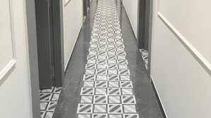 A long, narrow hallway with a patterned floor, white walls, and doors on both sides. - Hotel Trawika (Ahmedabad)