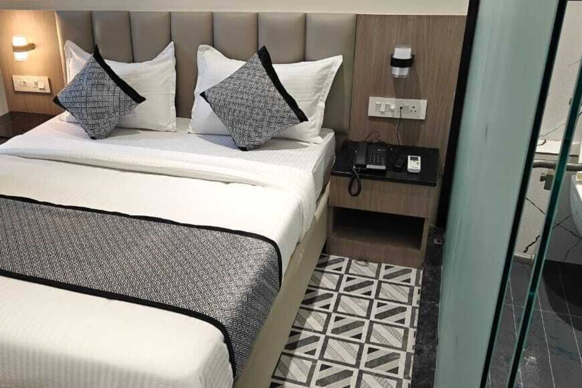 A hotel room with a bed, a bedside table with a phone, a mirror, and a bathroom with a sink and toilet.