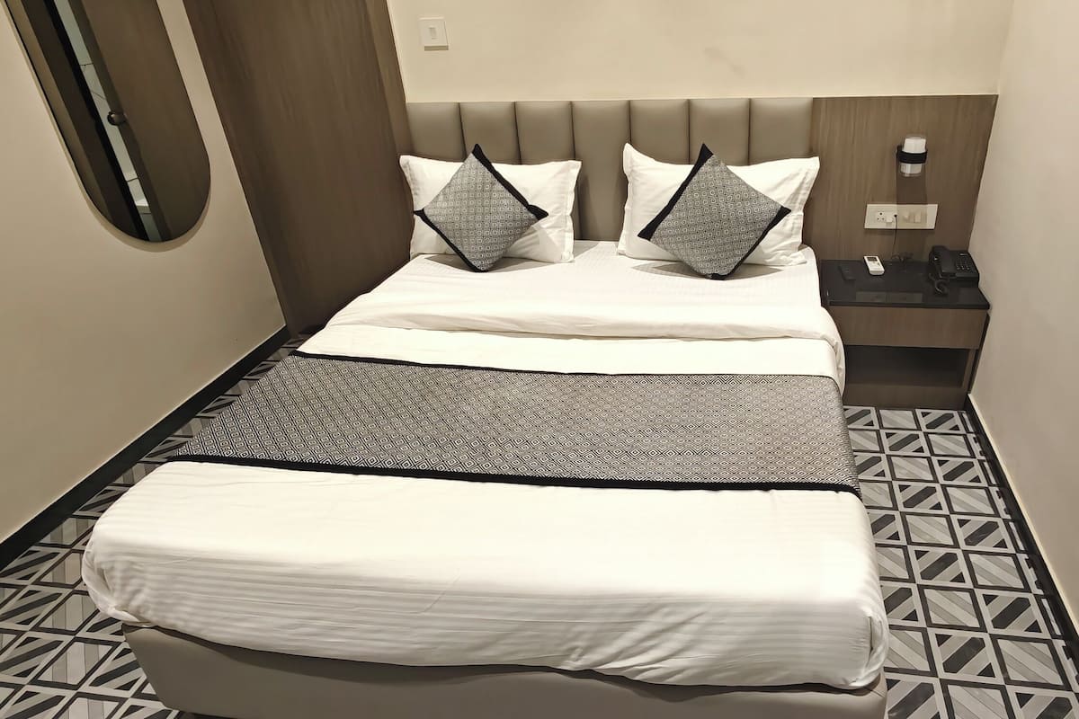 A hotel room with a bed, a bedside table with a phone, and a wall-mounted outlet.