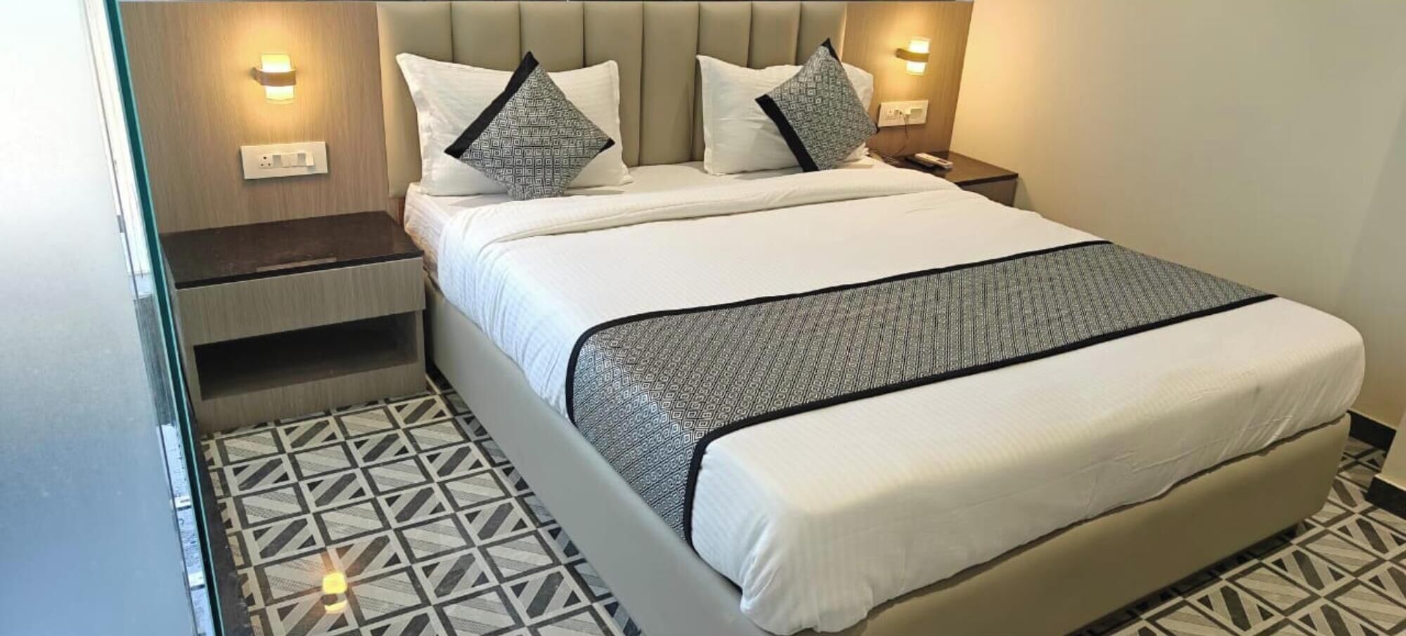 A hotel room with a bed, two bedside tables, and a patterned floor.