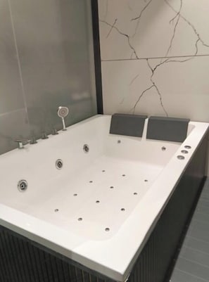 Une salle de bain moderne avec une grande baignoire rectangulaire, une cabine de douche en verre et un mur décoré d’un motif imitant le marbre.