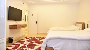 Una camera da letto con due letti, una TV a parete, una panca in legno e un tappeto decorato.
