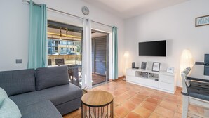 A modern living room with a grey sofa, a round wooden coffee table, a flat-screen TV, and a white entertainment unit.