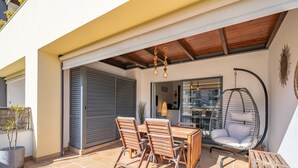 An outdoor patio with a wooden table and chairs, a hanging chair, and a sliding door.