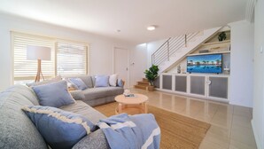 A modern living room with a grey sofa, a coffee table, and a TV on a white cabinet.