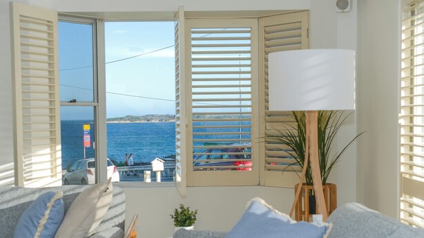A room with a view of the sea, a sofa with cushions, a lamp, and a small table.