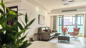 Una sala de estar moderna con un sofá, un sillón y una mesa de centro, un ventanal con cortinas y una planta en primer plano.