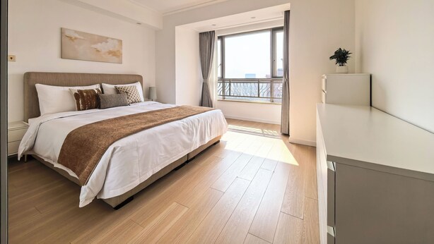 Un dormitorio moderno con una cama grande, una mesita de noche, una ventana con cortinas y vistas a la ciudad.