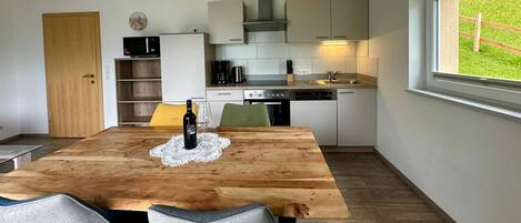 A compact kitchen with modern appliances, a dining table with chairs, and a window with a view of a green landscape.