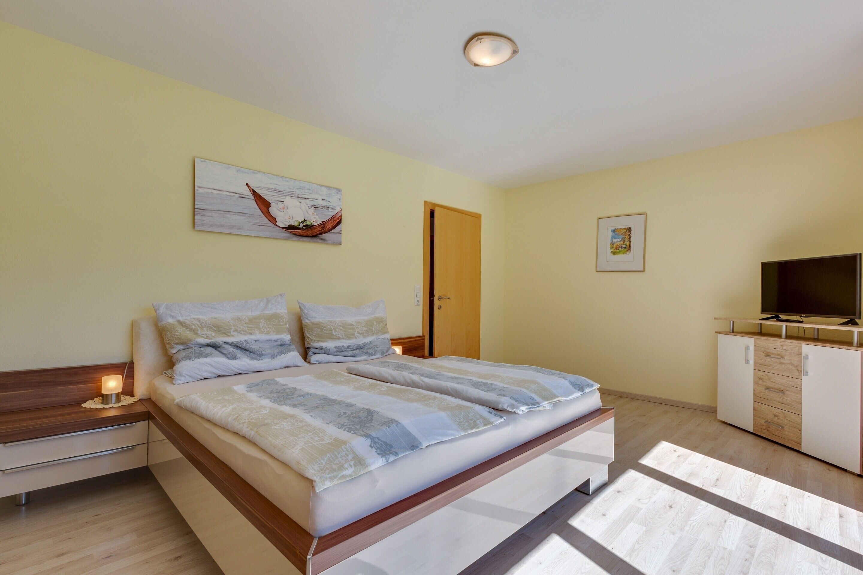 A bedroom with a bed, bedside tables, a television, and artwork on the walls.