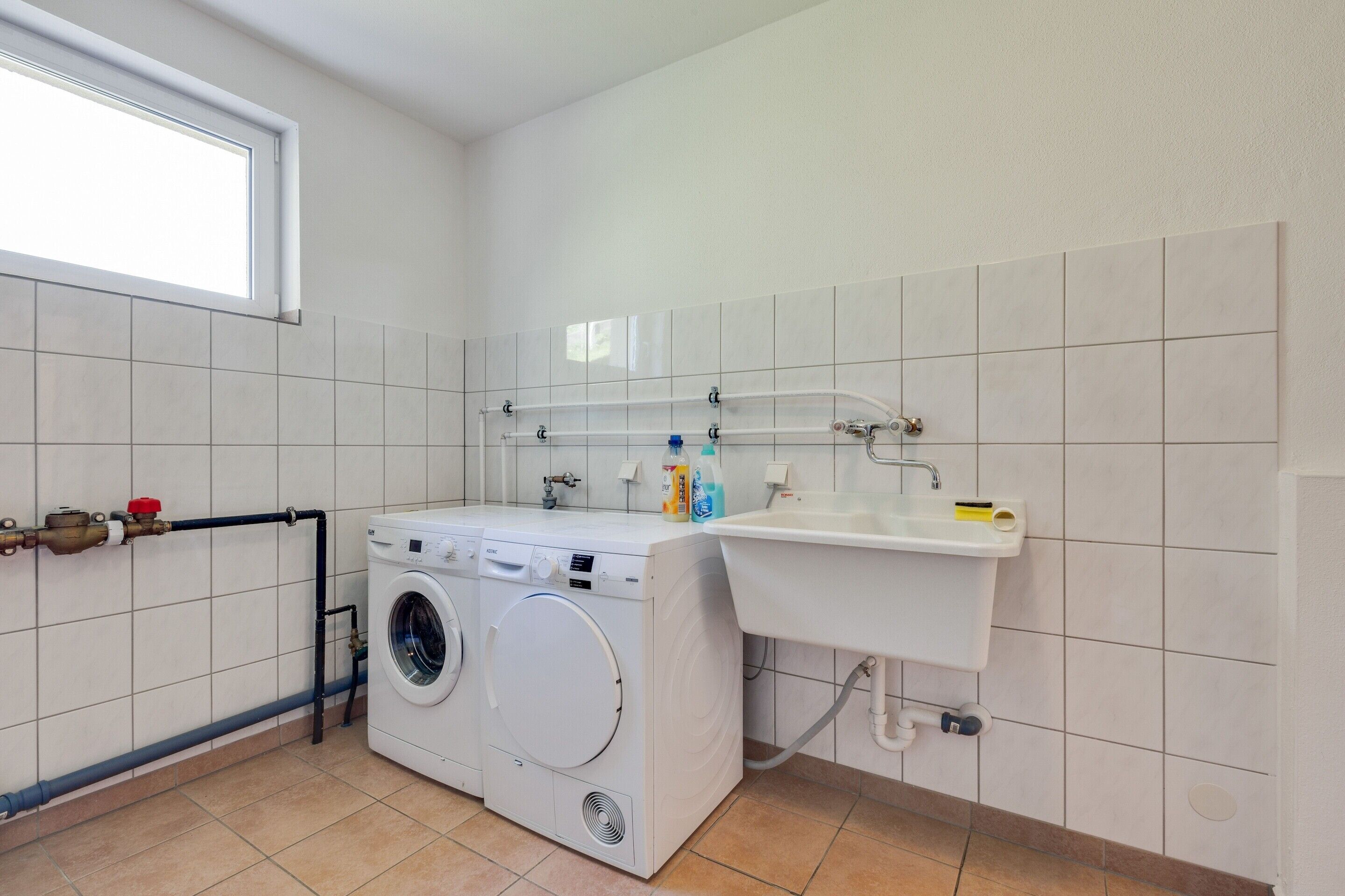A laundry room with a washing machine, a sink, and a window.