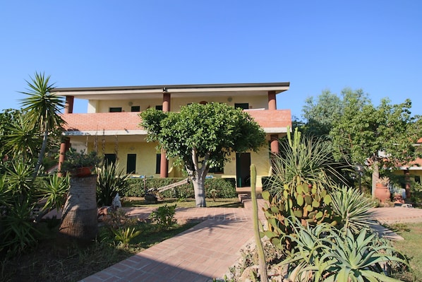 A building with a tiled roof and a garden with cacti and a palm tree. - Beachside Holiday Home in Ricadi (Ricadi)