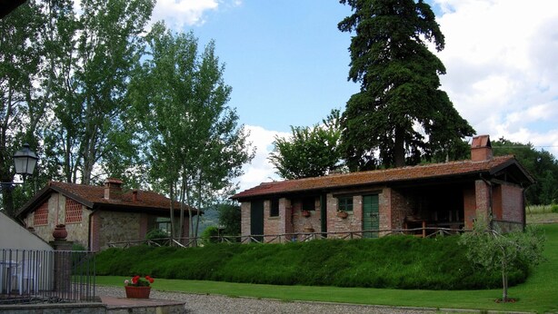 A rustic brick house with a sloped roof, a small porch, and a gravel driveway. - Farmhouse in Tuscany With Pool & Valley Views (Poppi)