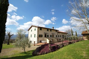 Une maison à deux étages avec un patio, entourée d’une clôture en bois et d’arbustes en fleurs.