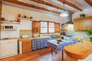 Una cocina compacta con armarios de madera, un microondas, un tostador y una mesa con un frutero y vasos.