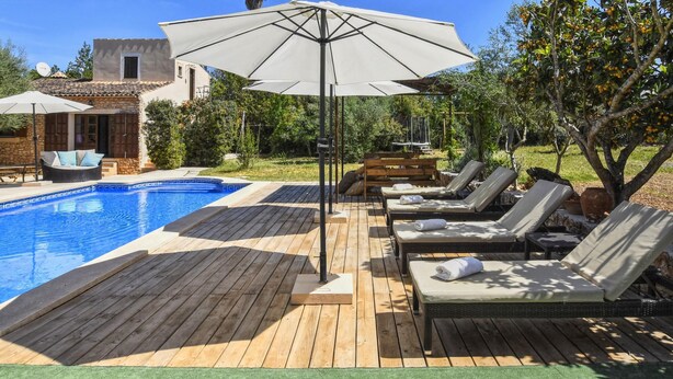 Une terrasse en bois avec une piscine, des chaises longues et des parasols.