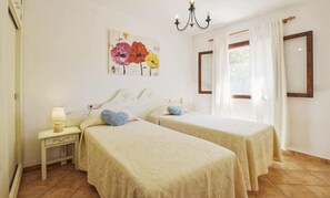 Une chambre avec deux lits, une table de chevet, une lampe, un tableau, un lustre et une fenêtre avec des rideaux.