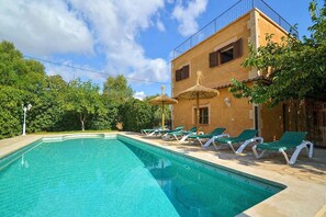 A swimming pool with lounge chairs and umbrellas, surrounded by greenery and a building with a balcony. - Villa in Manacor With Pool and Tennis Court (Manacor)