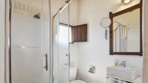 Une salle de bain avec une douche à parois de verre, des toilettes, un lavabo avec un miroir et un meuble de rangement.