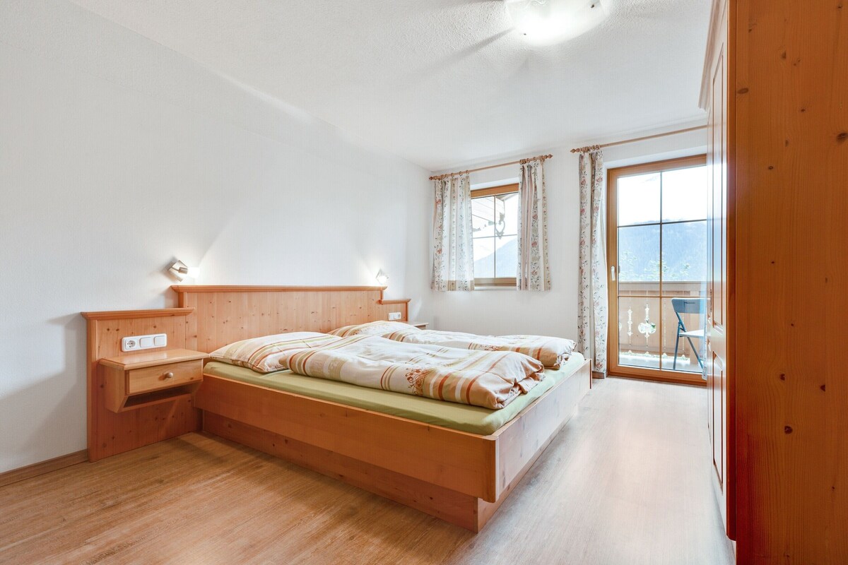 A bedroom with a wooden bed, bedside tables, a window with curtains, and a view of the outdoors.