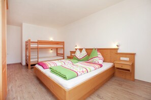 A bedroom with a bunk bed, a single bed with a colorful bedspread, a nightstand, and a wall-mounted shelf. - Chalet in Mittersill Near Ski Slopes (Mittersill)