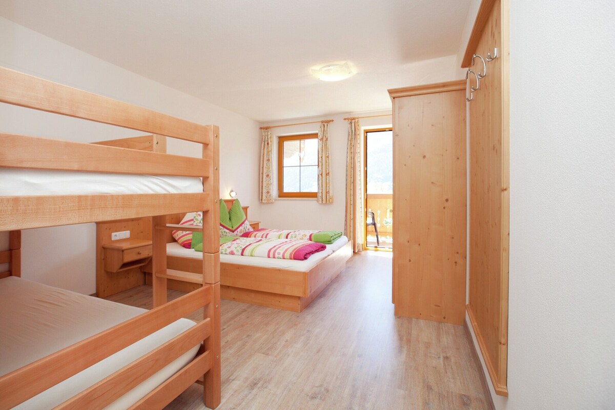 A bunk bed room with a wooden wardrobe and a window with curtains.