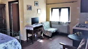 Una camera accogliente con un letto, una scrivania con un computer, una sedia, una finestra e un angolo cottura.