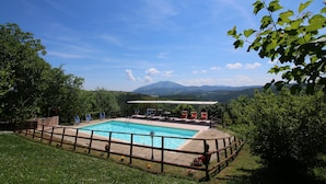 Una piscina con bordo in legno, circondata da una recinzione, con vista su un paesaggio montuoso.