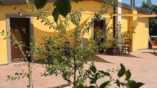 Un edificio giallo con una porta e finestre, un tavolino con sedie e un albero sullo sfondo.