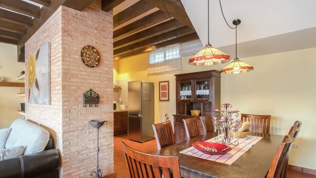 A dining area with a brick column, wooden chairs, a table with a red bowl, and hanging pendant lights.