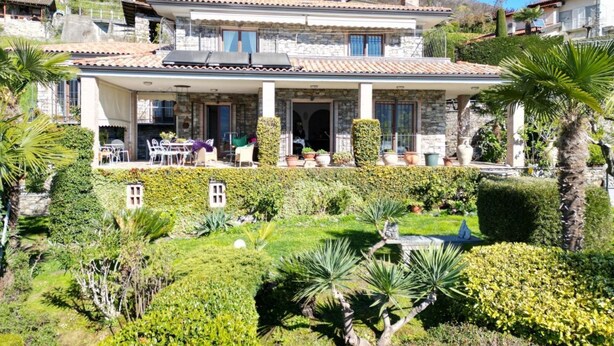 Ein zweistöckiges Haus mit einer Terrassenfläche, umgeben von gepflegten Gärten und einem Pool.