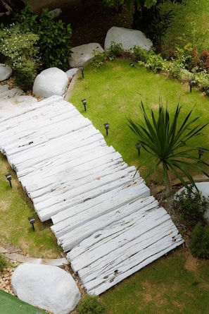 Un sendero de madera blanca en un jardín con rocas y plantas.