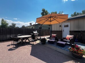 A patio with outdoor furniture, a grill, and a large umbrella.