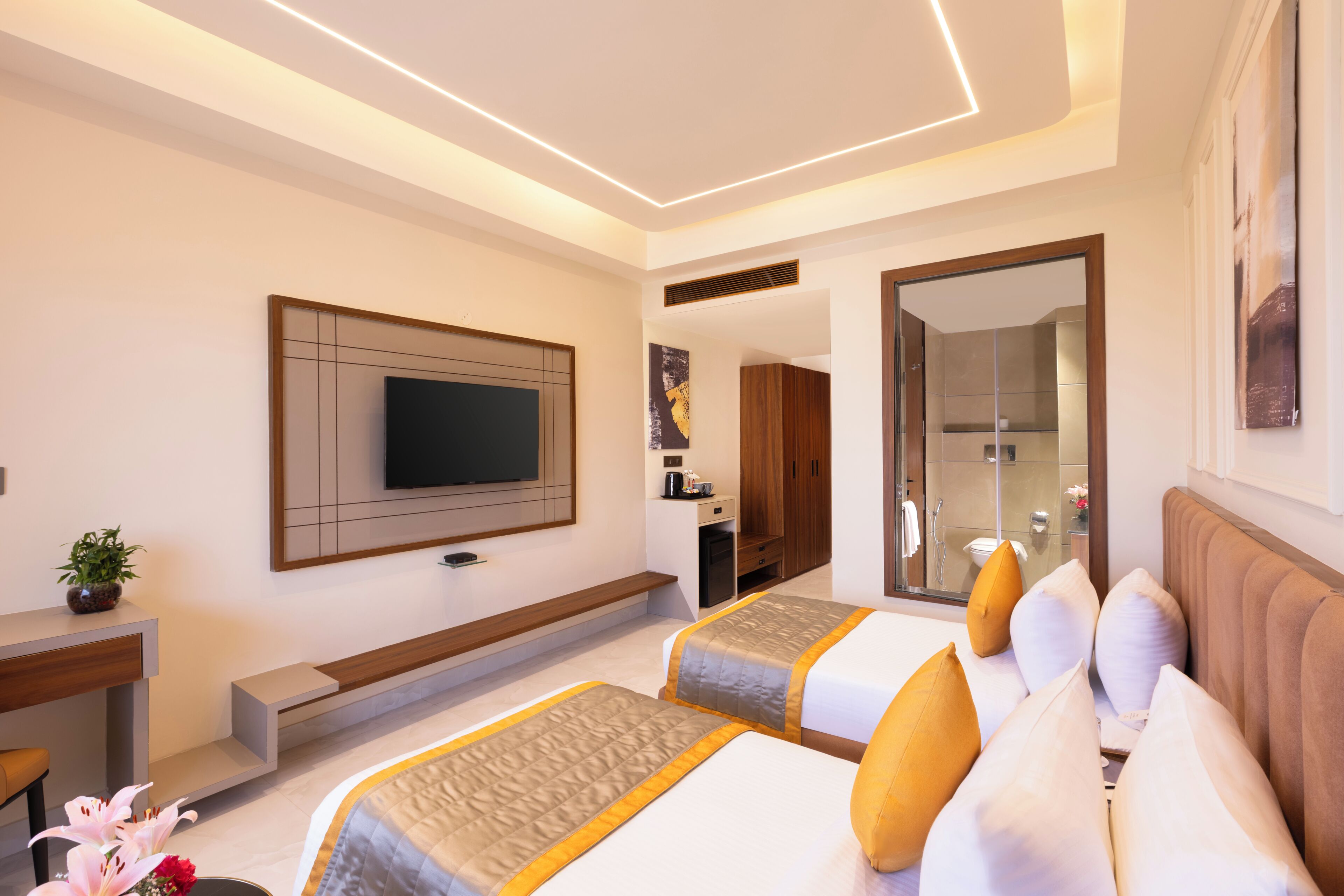 Une chambre d’hôtel moderne équipée d’un téléviseur à écran plat, d’un bureau, d’un canapé et d’une salle de bain visible à travers une porte ouverte.