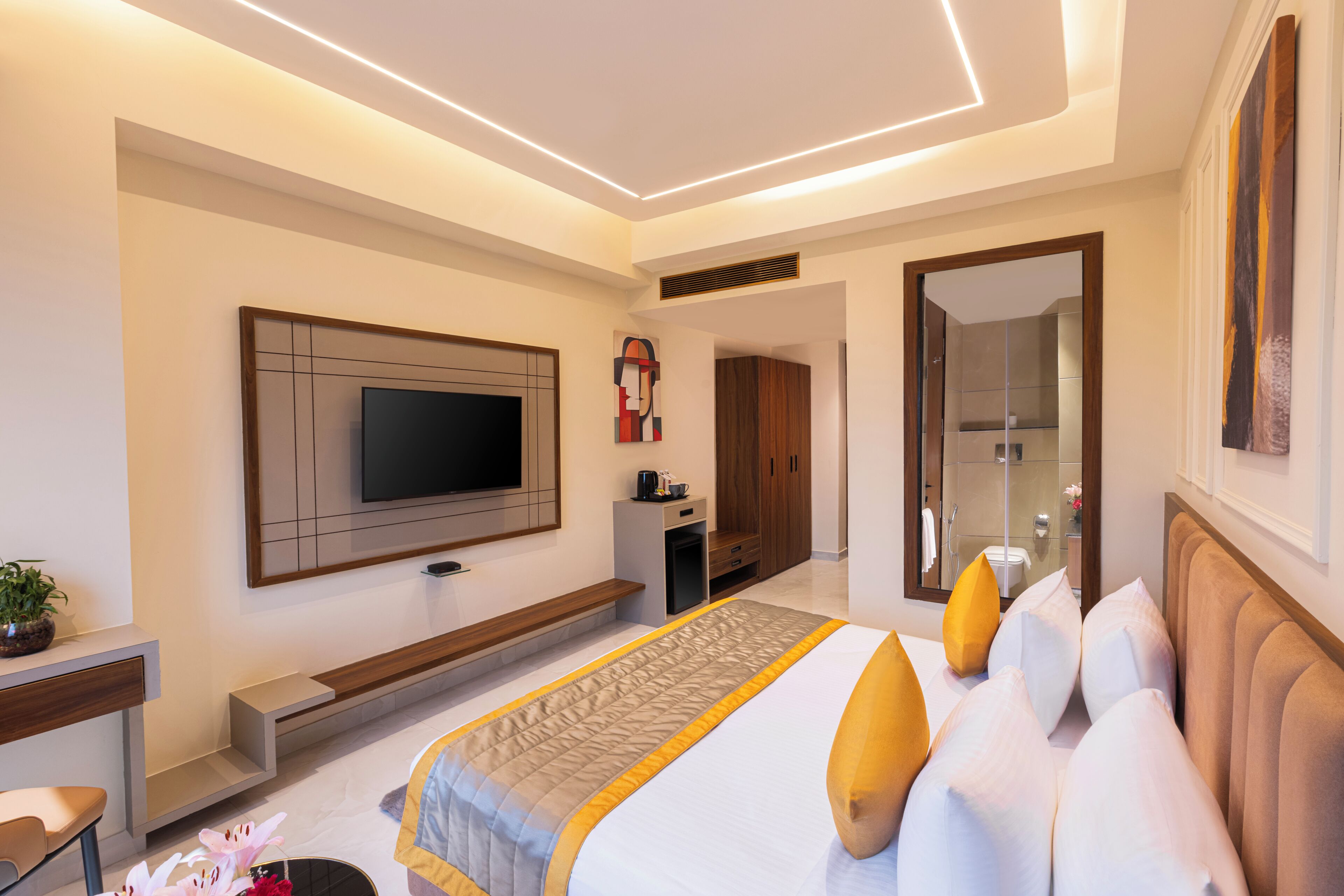 A modern hotel room with a large bed, a flat-screen TV, a bench, and a bathroom visible through an open door.