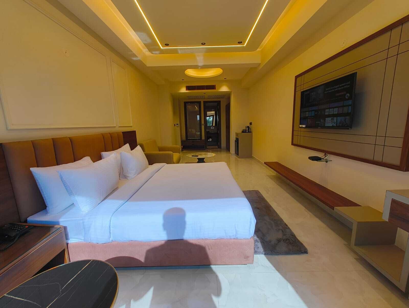 A modern hotel room with a large bed, a TV mounted on the wall, and a small desk.