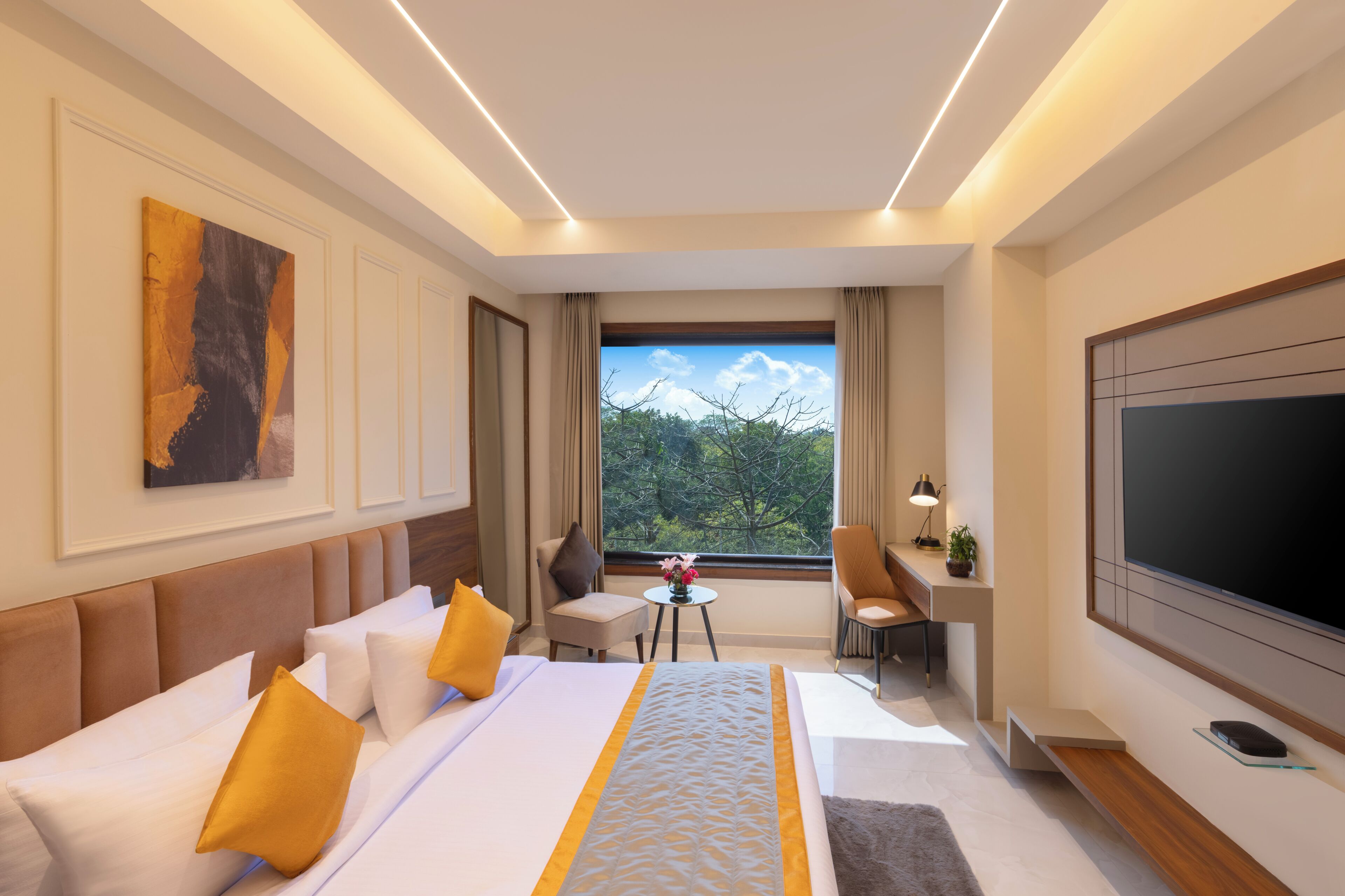 A hotel room with a bed, a desk, a chair, a TV, and a window with a view of trees.