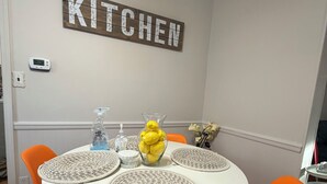 Uma sala de jantar com uma mesa branca, cadeiras laranja, um letreiro 'KITCHEN' e um vaso com limões.