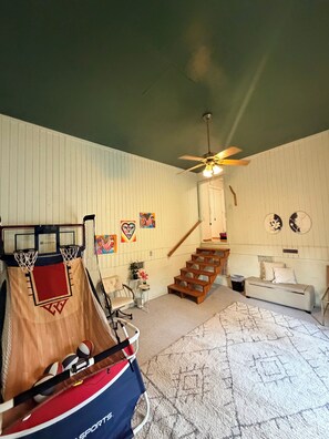 Ein Zimmer mit Basketballkorb, einer Treppe, einer Couch und einem Deckenventilator.