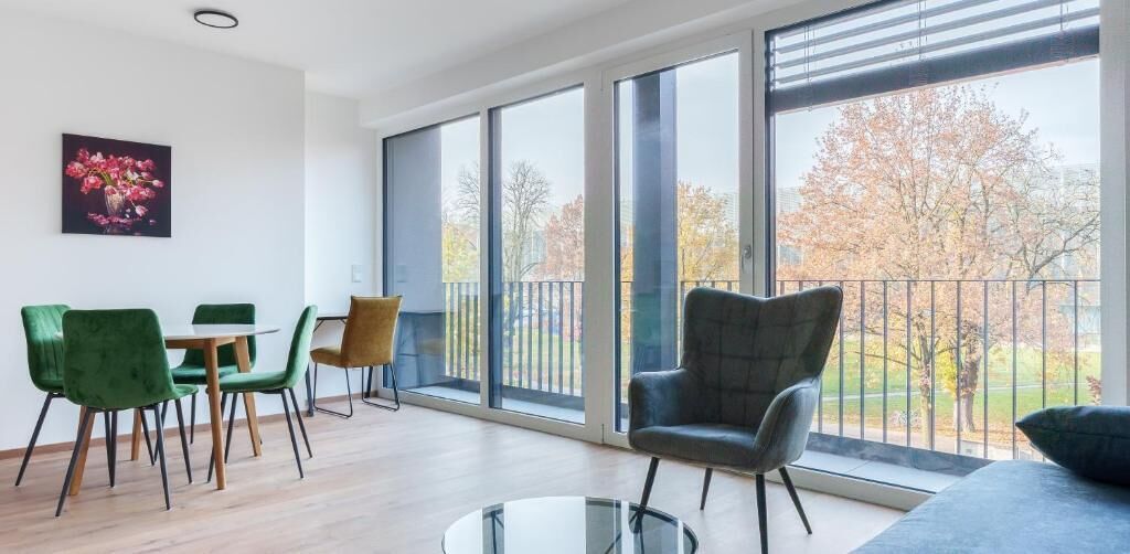 En moderne stue med store vinduer, et spiseområde med grønne stole og en grå lænestol.