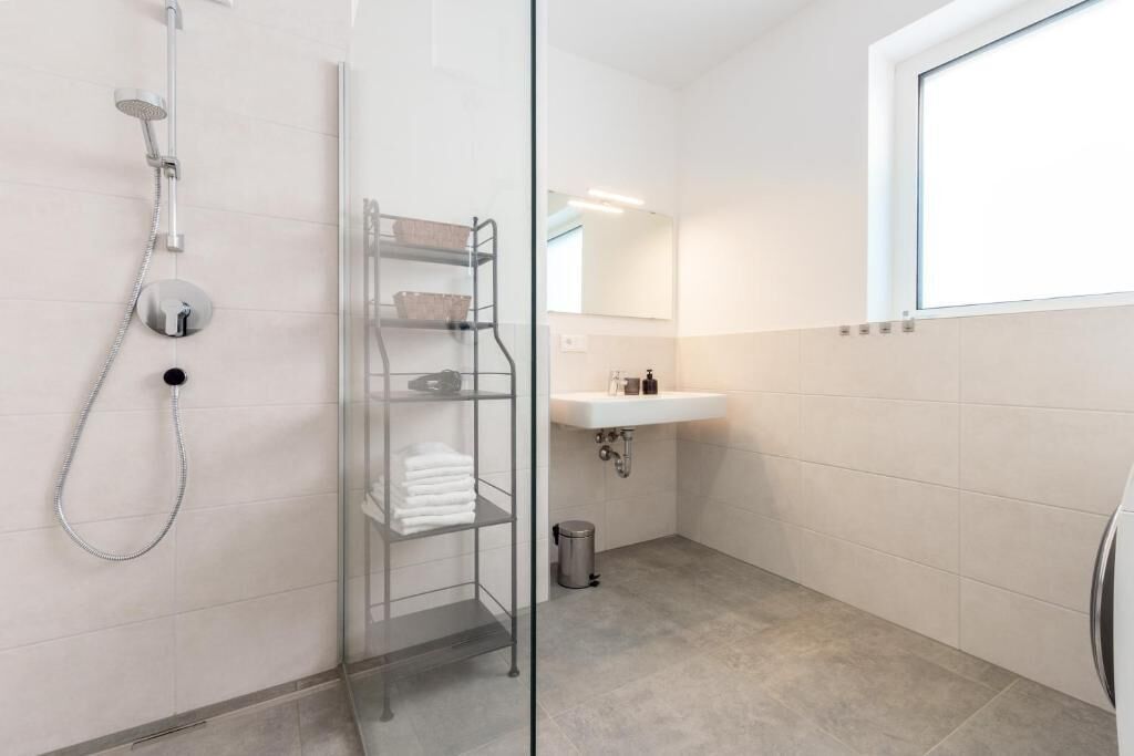 A modern bathroom with a glass shower enclosure, a white sink, and a mirror above it.
