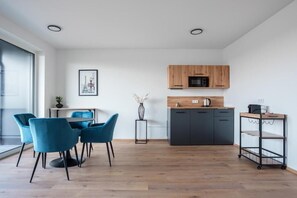 Une cuisine moderne avec des meubles en bois, un four à micro-ondes et une machine à café. On y trouve également un coin repas avec des chaises bleues et une petite table.