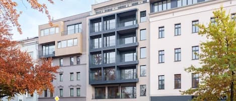 A modern multi-story building with a mix of residential and commercial spaces, featuring balconies, large windows, and a clean, contemporary design.