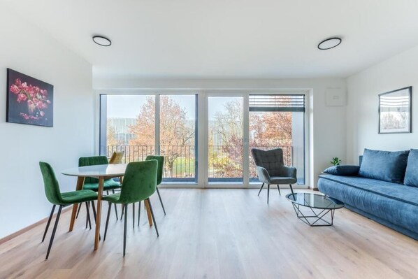 Un salon moderne avec un coin repas, de grandes fenêtres et un canapé bleu.
