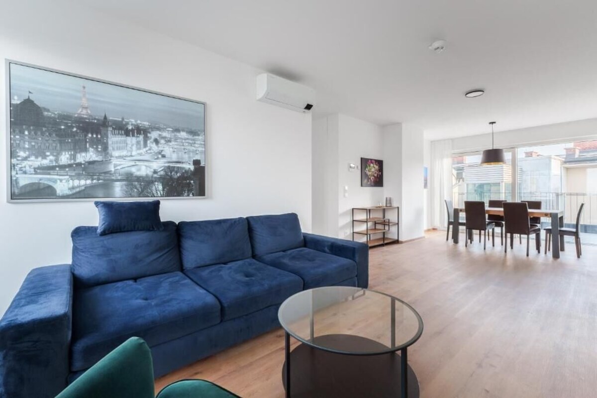 A modern living room with a blue sofa, a glass coffee table, and a dining area with a table and chairs.