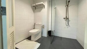 Un baño pequeño y moderno con azulejos blancos, un inodoro, cabina de ducha de vidrio y un perchero para toallas.